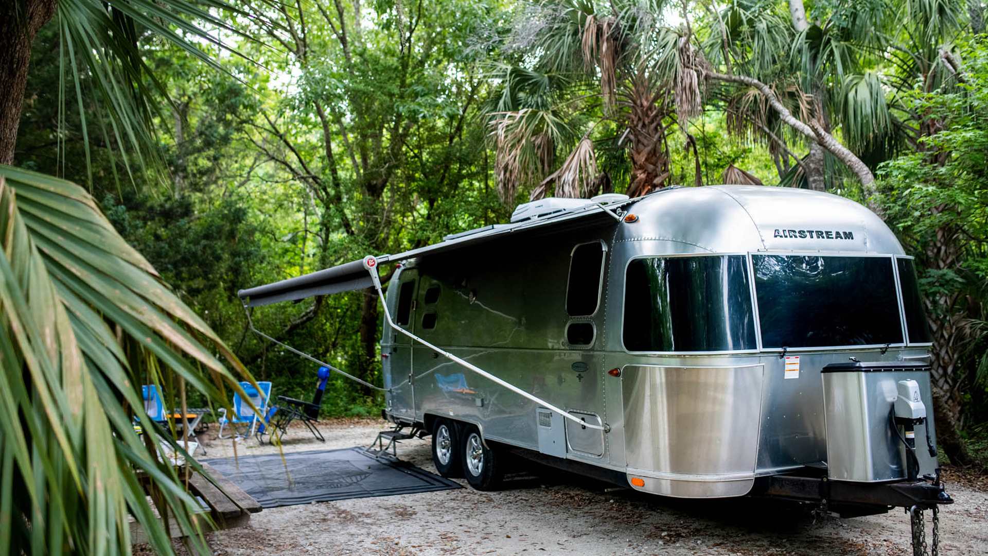 An Airstream travel trailer parked in a tropical place with its Zip-Dee Awning out.