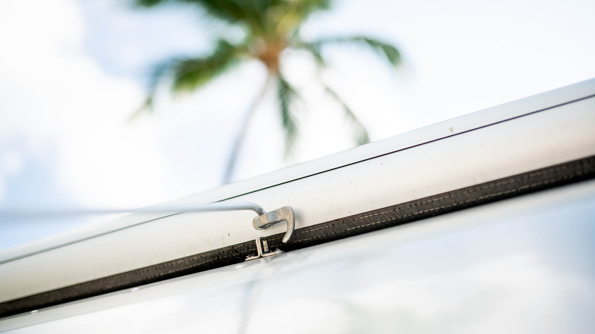 A man flipping the hook for his Zip Dee awning with the tool on his Airstream travel trailer while parked next to a palm tree