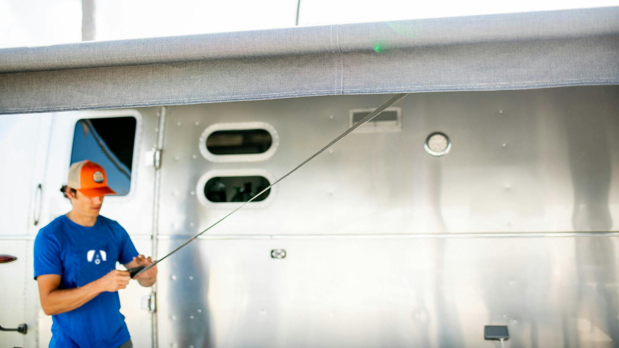 A man rolling out his Zip-Dee awning on his Airstream Travel Trailer