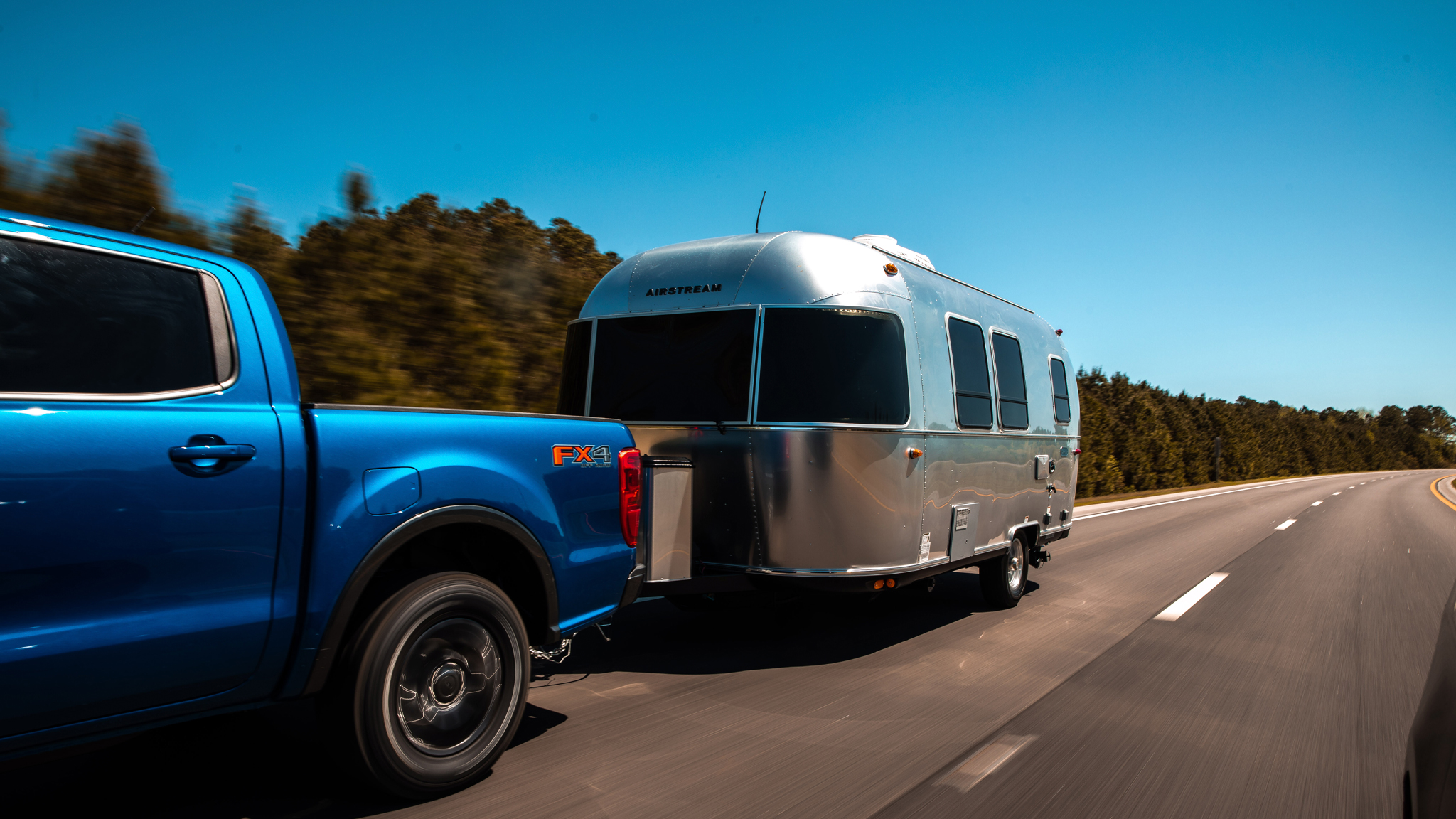 Blue-truck-towing-an-Airstream-trailer-while-driving-down-the-road