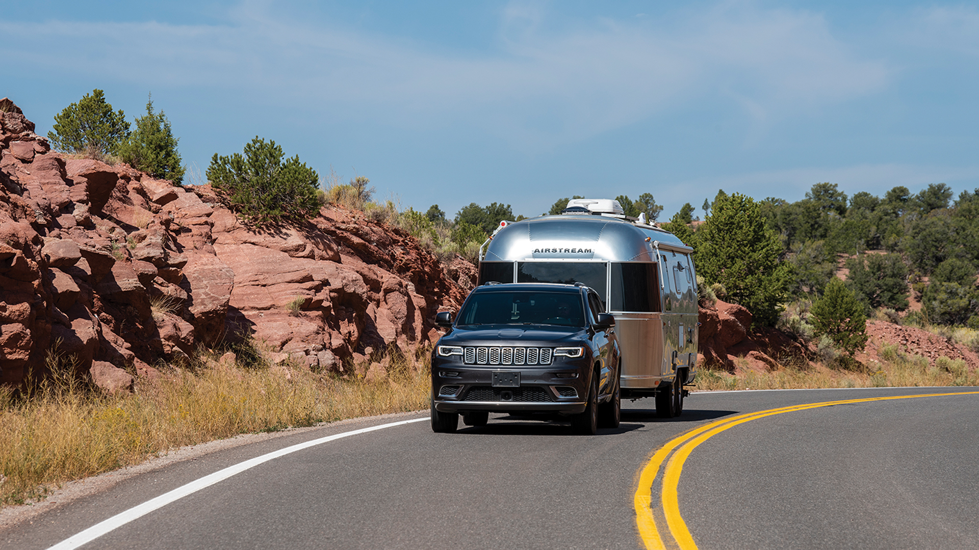 A SUV vehicle towing an Airstream travel trailer down a road.