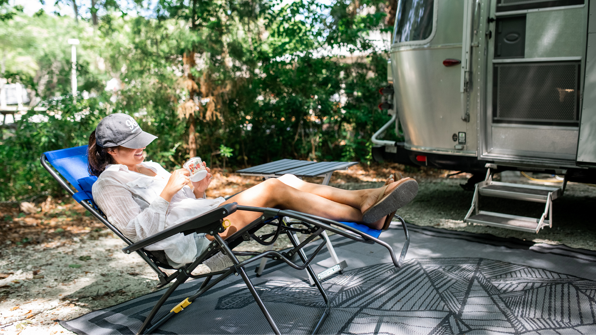 Danielle sitting in a lawn chair next to her Airstream Travel Trailer at a campground