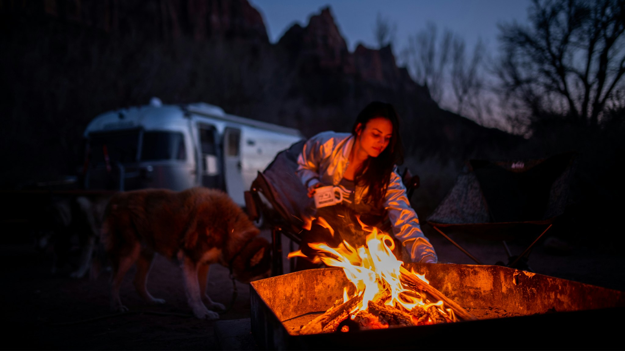 A woman sitting by a campfire with her dog