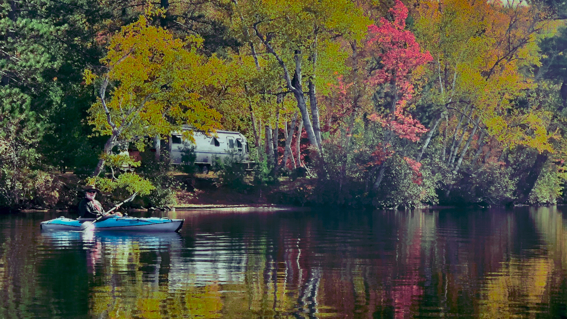 Jim canoeing in river with Airstream in the background