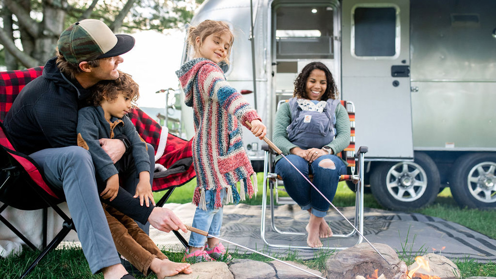 People outside of their Airstream Travel Trailer cooking food over a fire