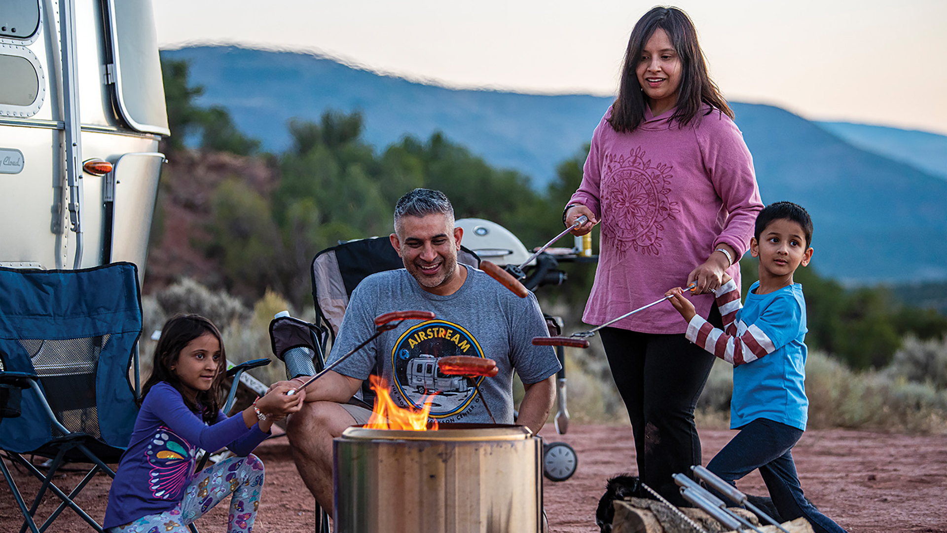 People outside of their Flying Cloud cooking hot dogs over a fire