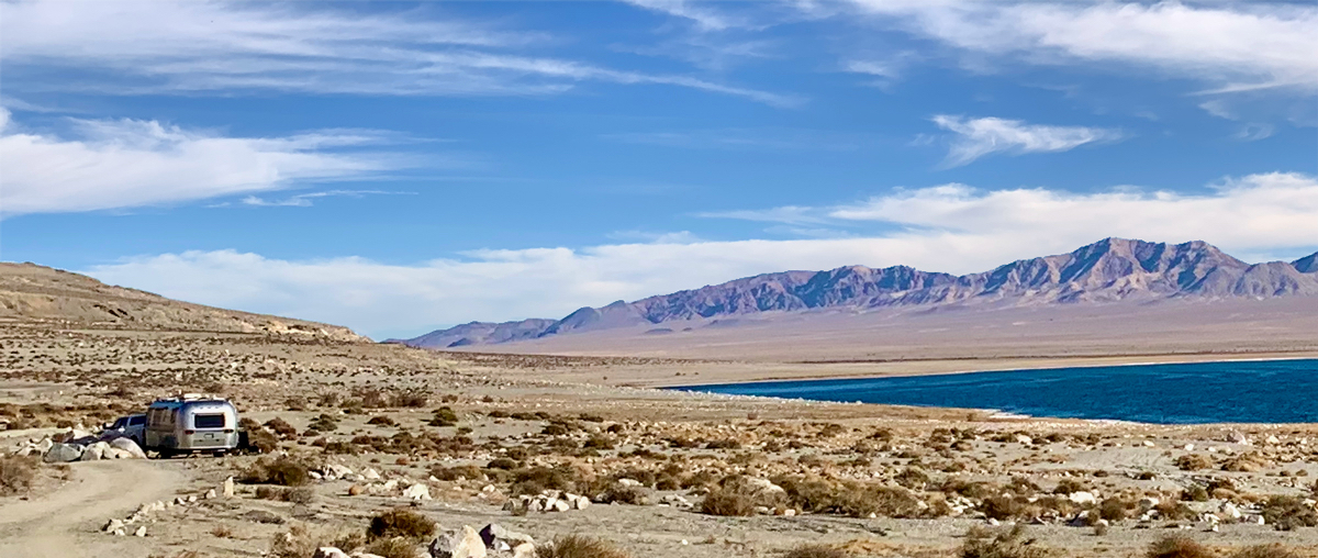 A 2001 Airstream travel trailer parked by a lake and mountains.