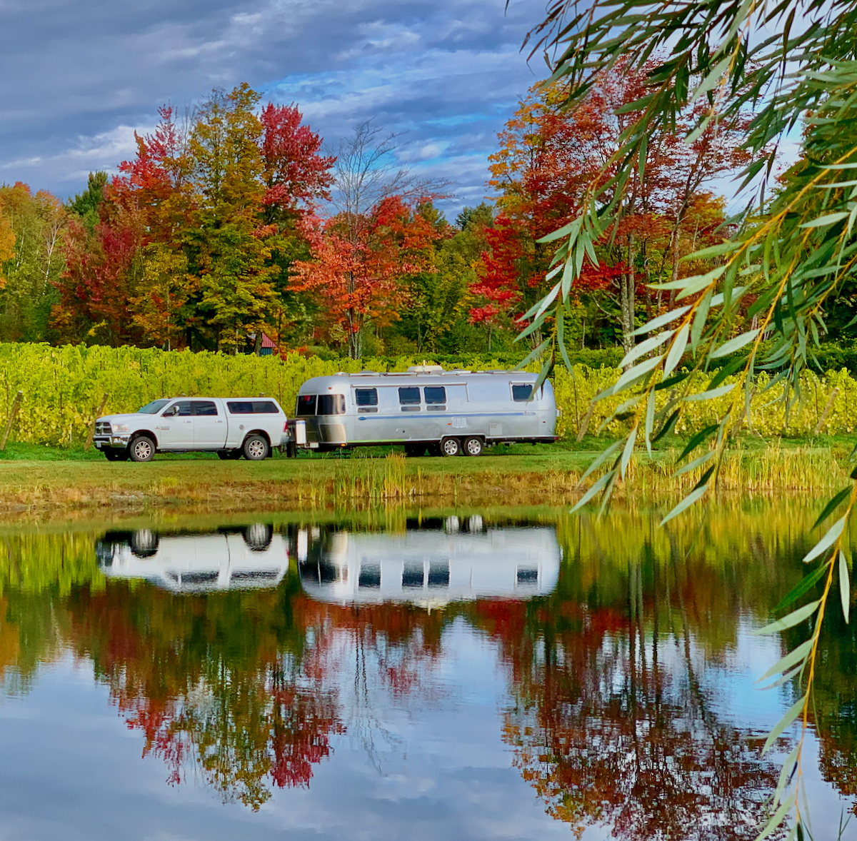 Airstream travel trailer being towed by a lake and woods during the fall.