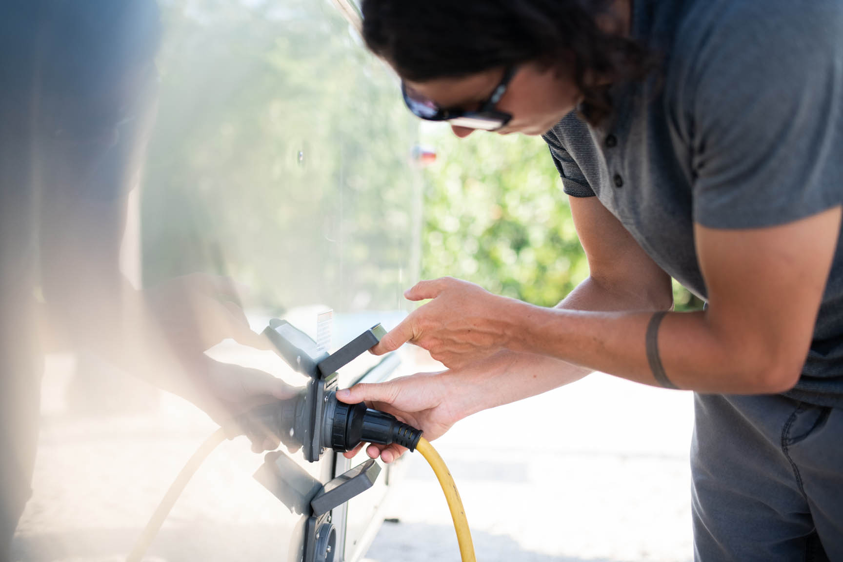 A man pluggung in an electrical cord to the outside of his Airstream travel trailer.