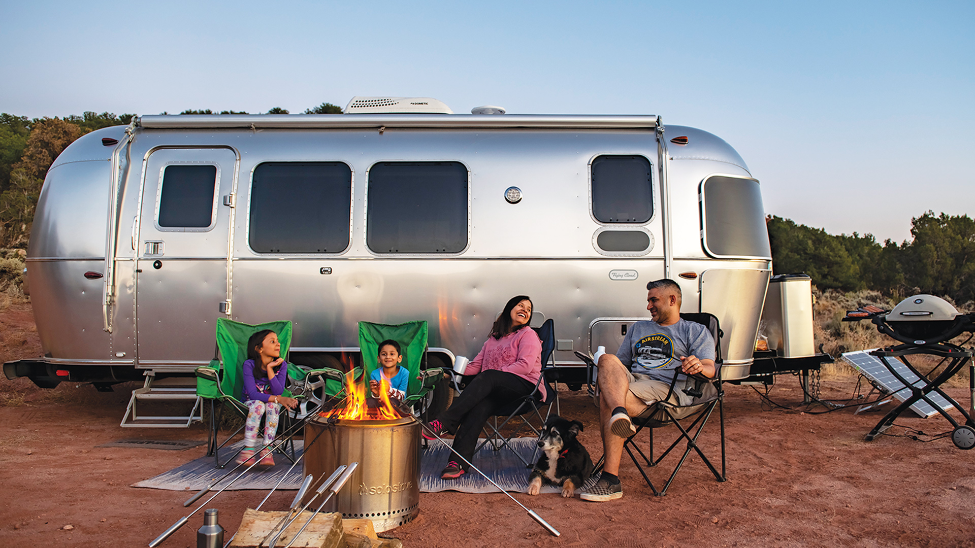 airstream flying cloud travel trailer with family sitting by the campfire in the desert