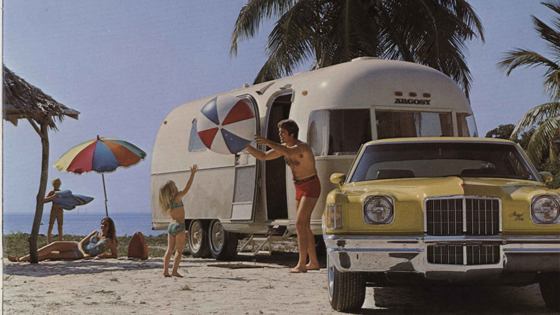 Airstream Argosy at the beach with a car towing and family playing outside