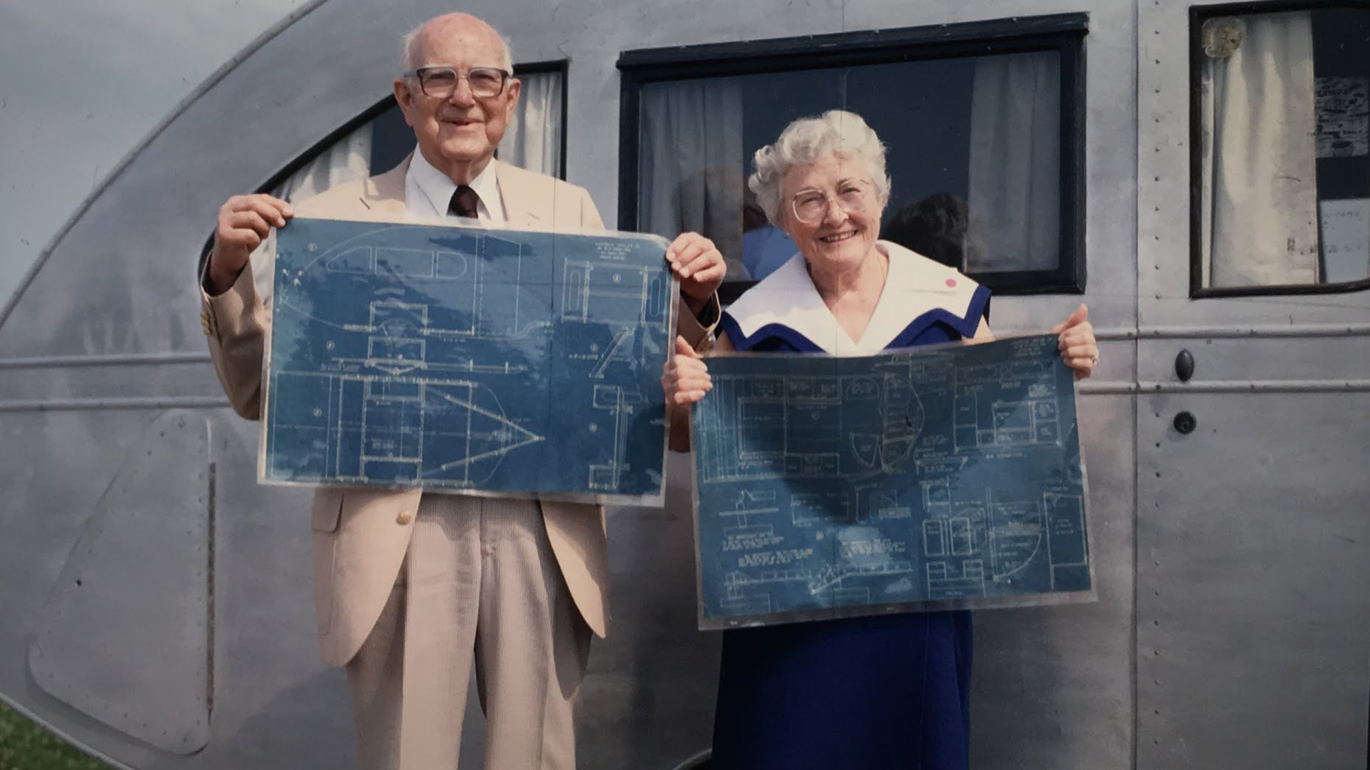 Dr. and Mrs. Holman holding up the Airstream Torpedo travel trailer blueprint while standing in front of the Airstream trailer