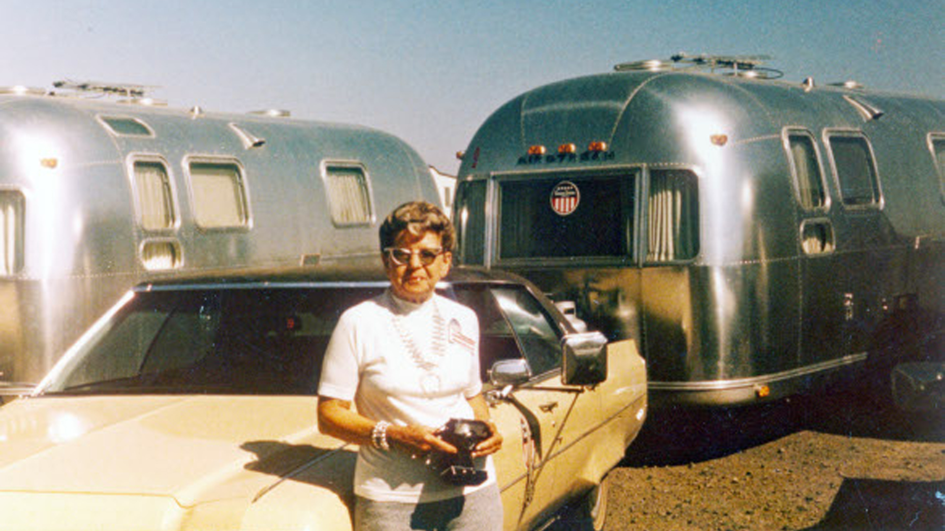 Helen Byam smiling for a picture next to two Airstream travel trailers and a white car