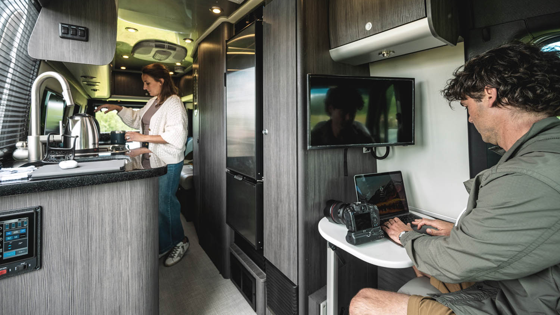 A couple inside their Airstream 24GT Touring Coach working at the desk and making coffee in the kitchen