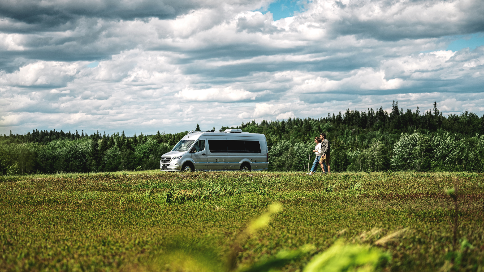 Airstream Interstate Touring Coach parked in a field with a couple walking outside.