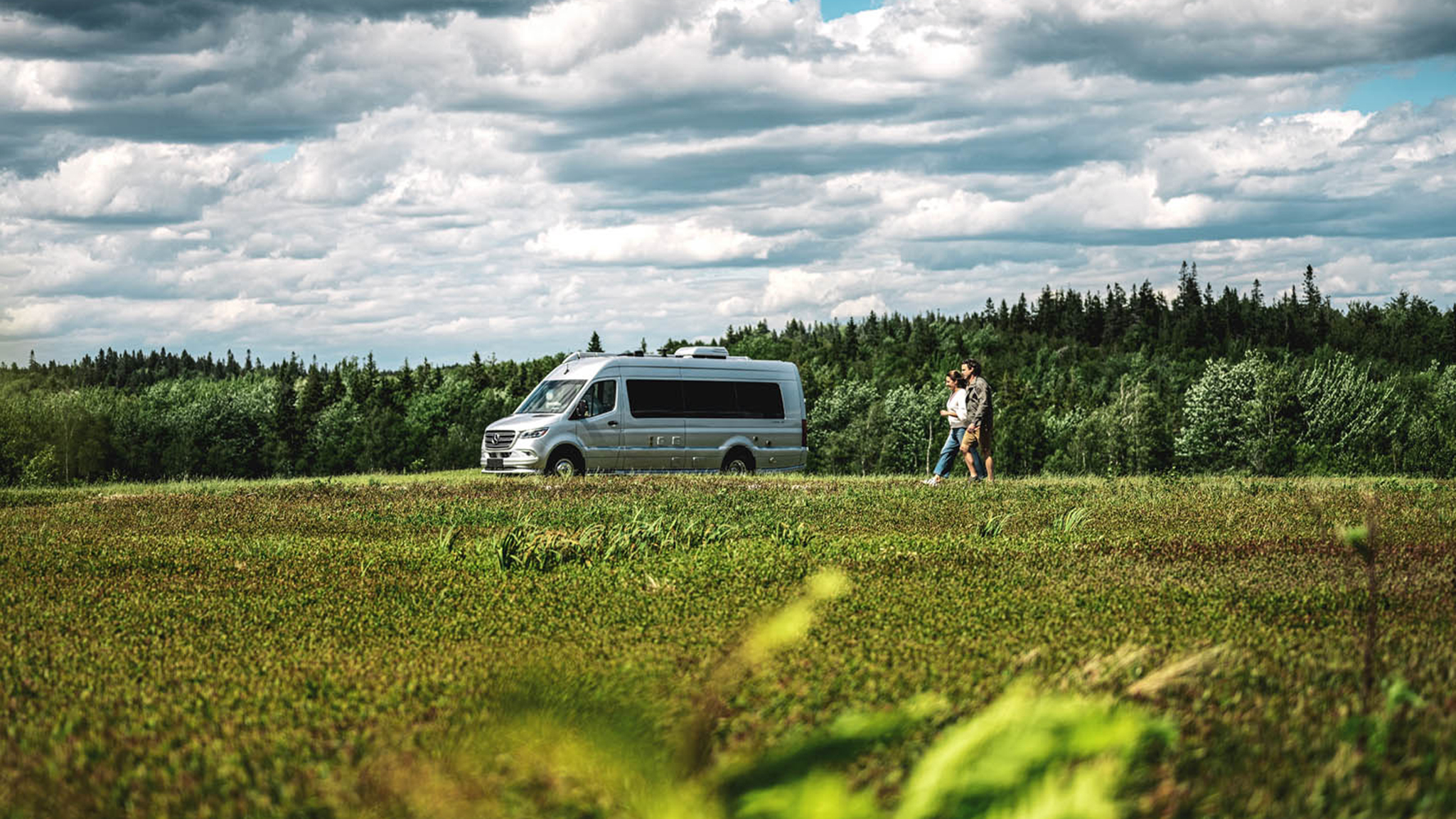 Airstream Interstate Touring Coach parked in a field with a couple walking outside.