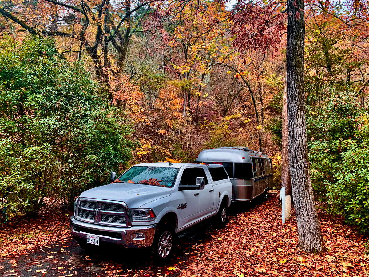 An Airstream Classic Travel Trailer being towed in a woods during the fall with colorful leaves.