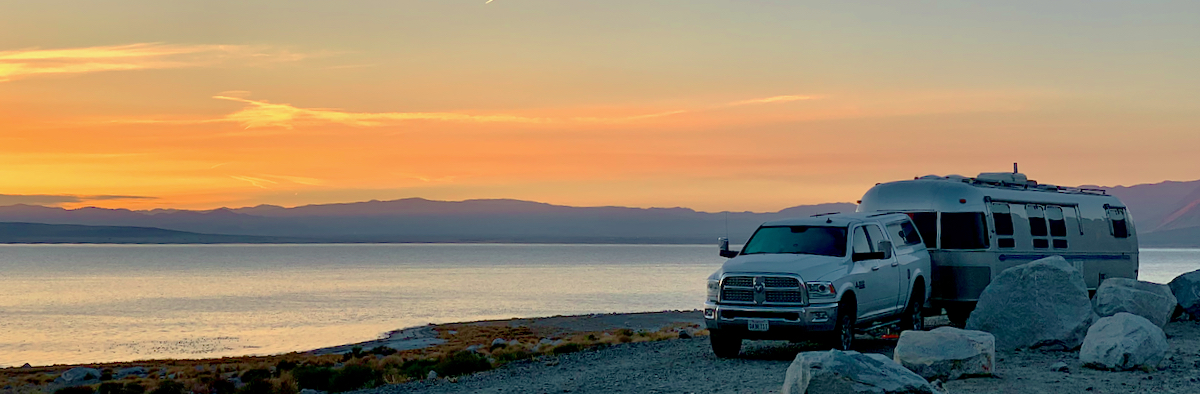 An Airstream Classic Travel Trailer being towed next to a beach while the sun is rising over the water