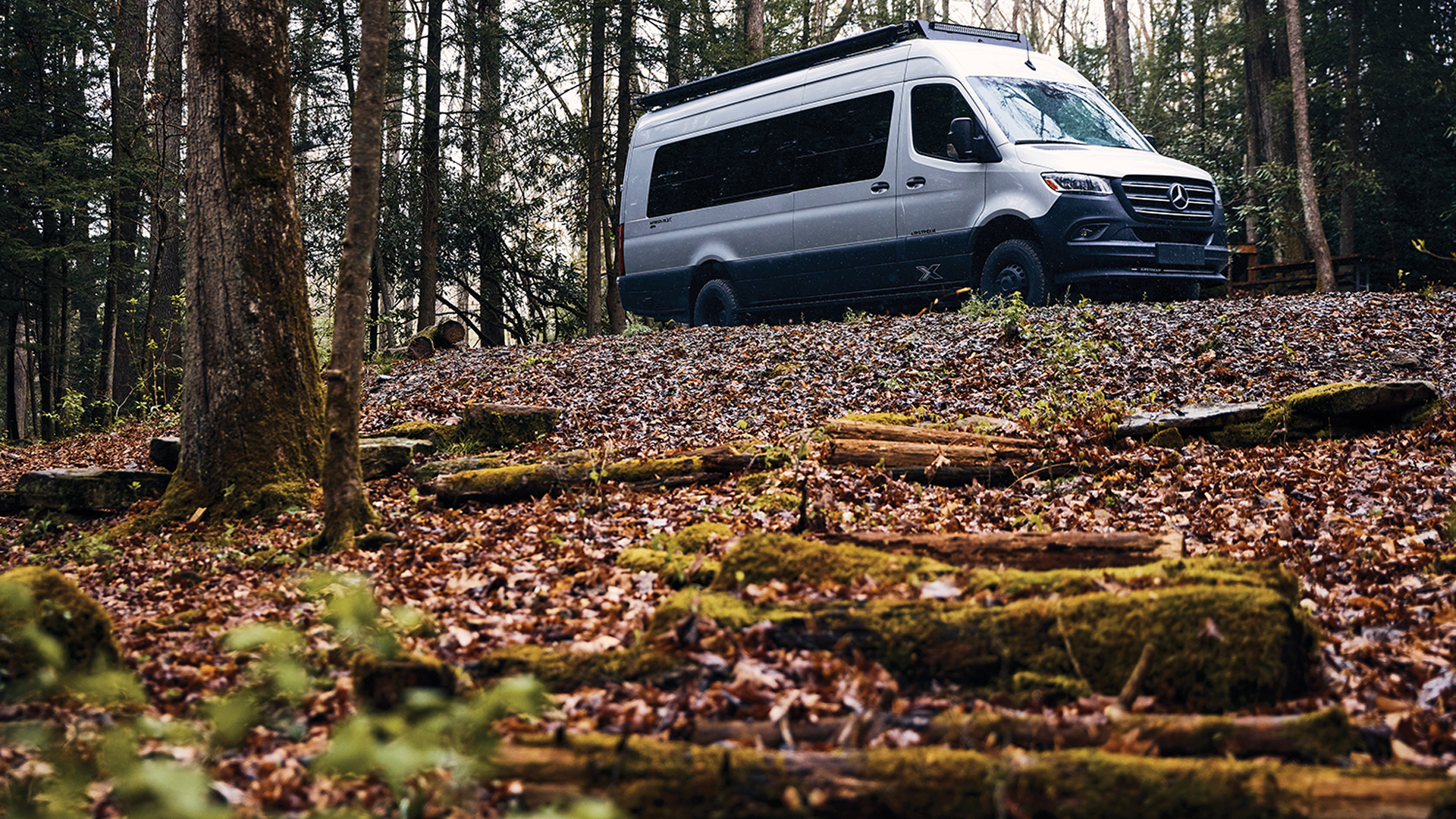 Airstream Interstate 24X Touring Coach driving off the road in a woods in the fall.