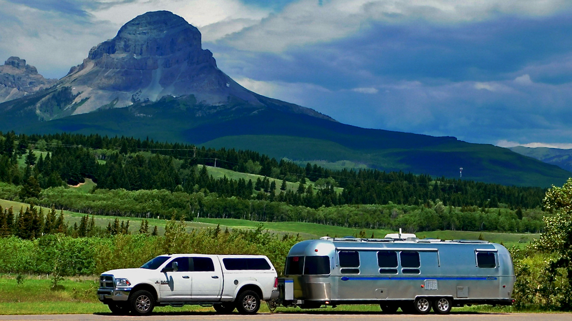 An airstream classic travel trailer being towed by a truck through a National Park with mountains in the background.