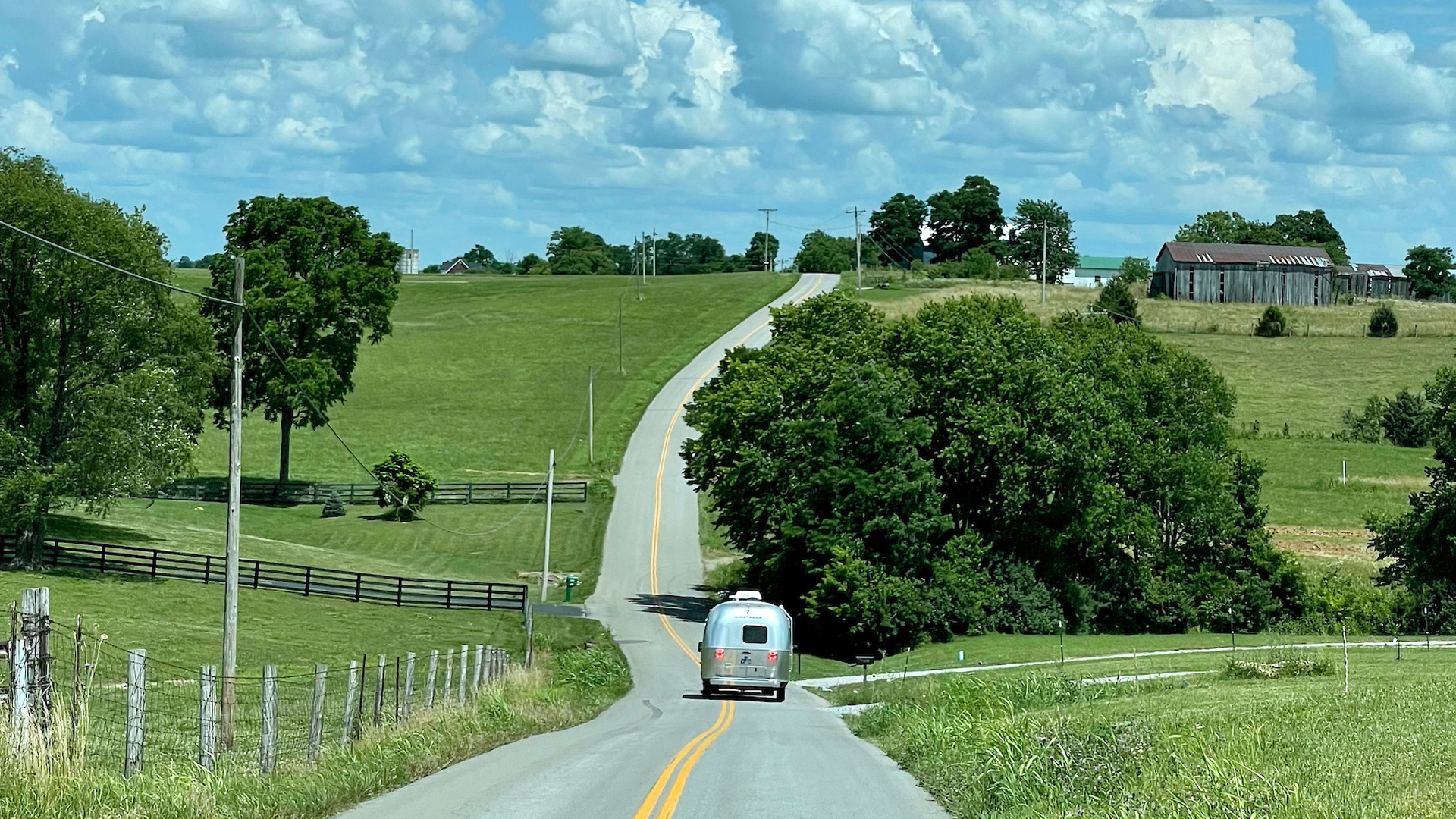 An Airstream Flying Cloud travel trailer being towed down the road on a countryside with lots of hills and trees.