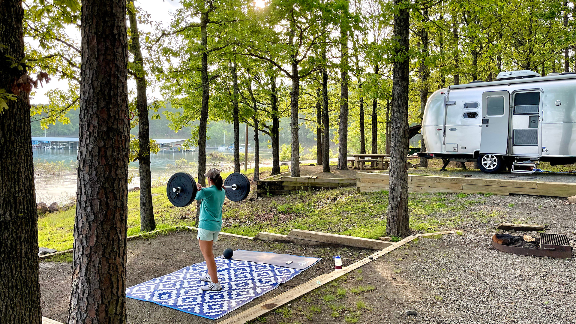 Dorsey Addicks lifting weights outside of her Airstream travel trailer that is parked next to a lake.
