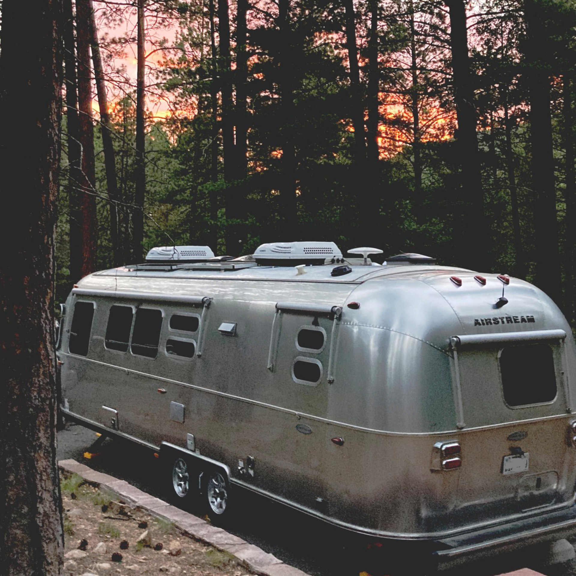 Airstream travel trailer parked next to trees during a sunset that is orange and pink.
