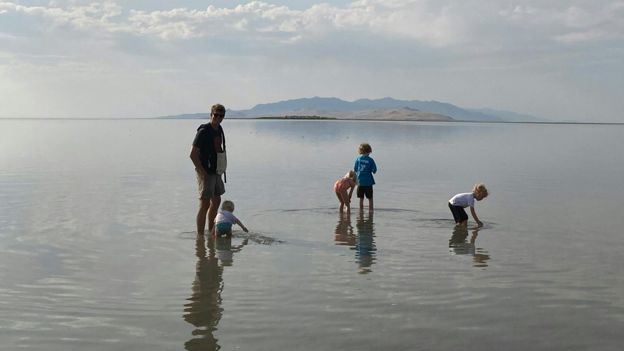 A family walking and playing in shallow water with a fog in the background.