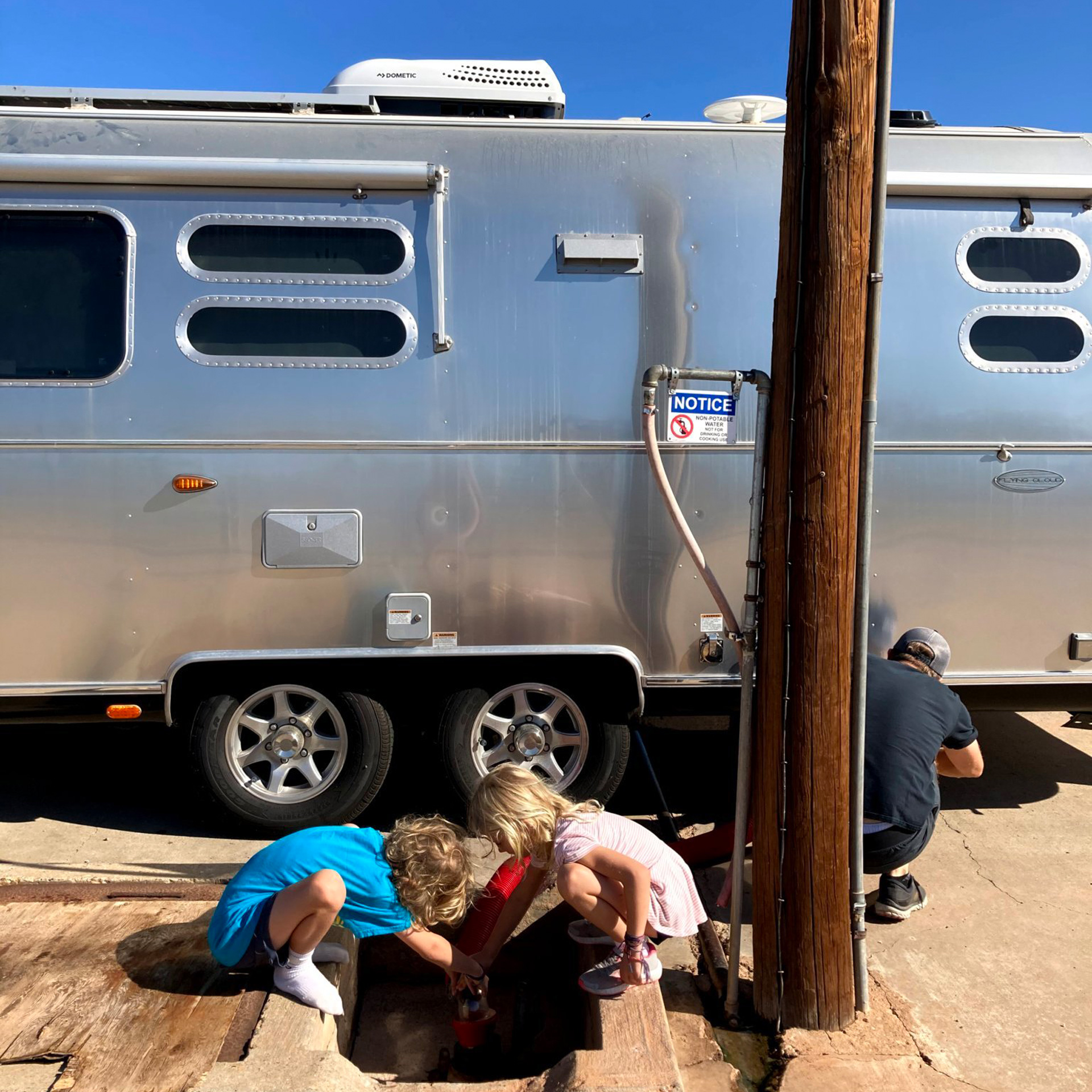 2 kids hooking up Airstream travel trailer with their dad in the desert.