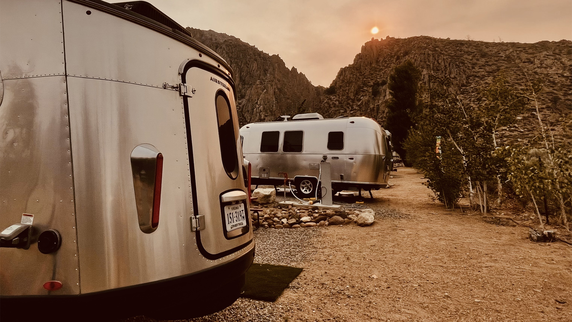 An Airstream Basecamp travel trailer parked next to another Airstream travel trailer at a campground out west.