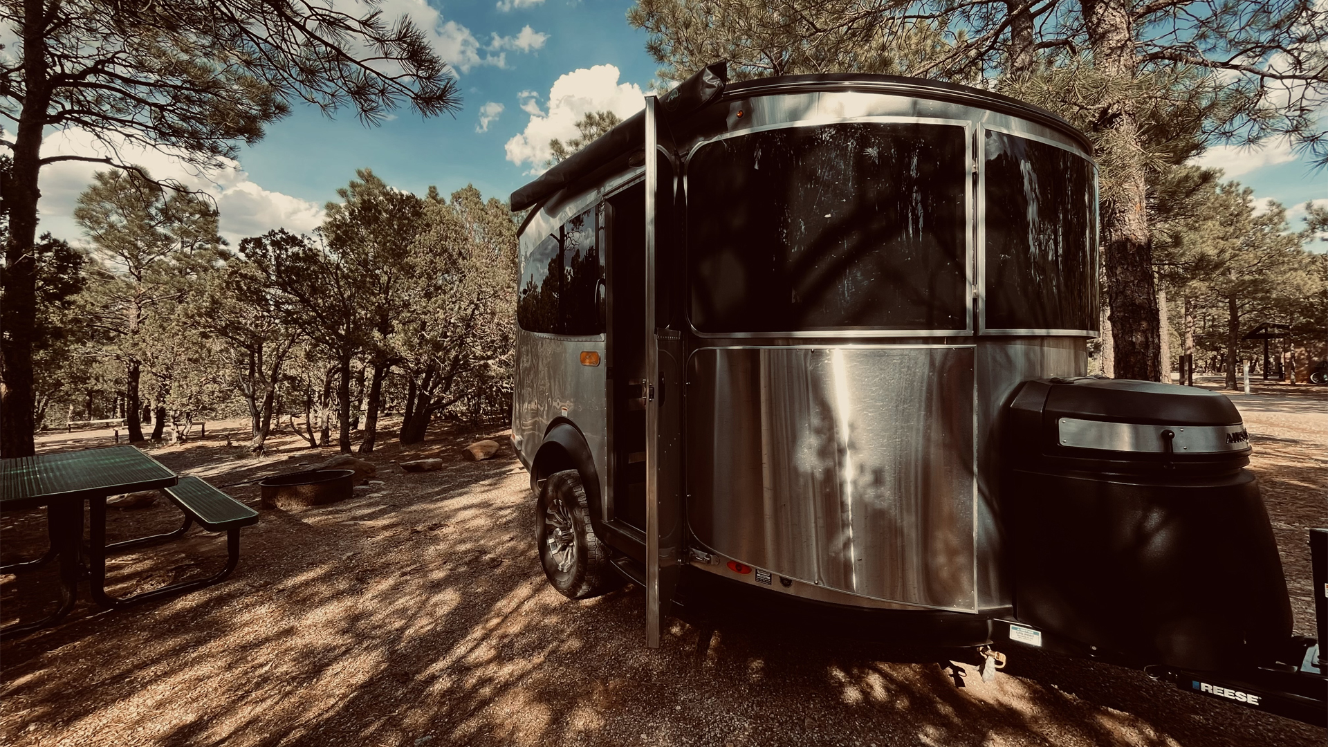 Airstream Basecamp travel trailer parked at a campground under a tree out west.