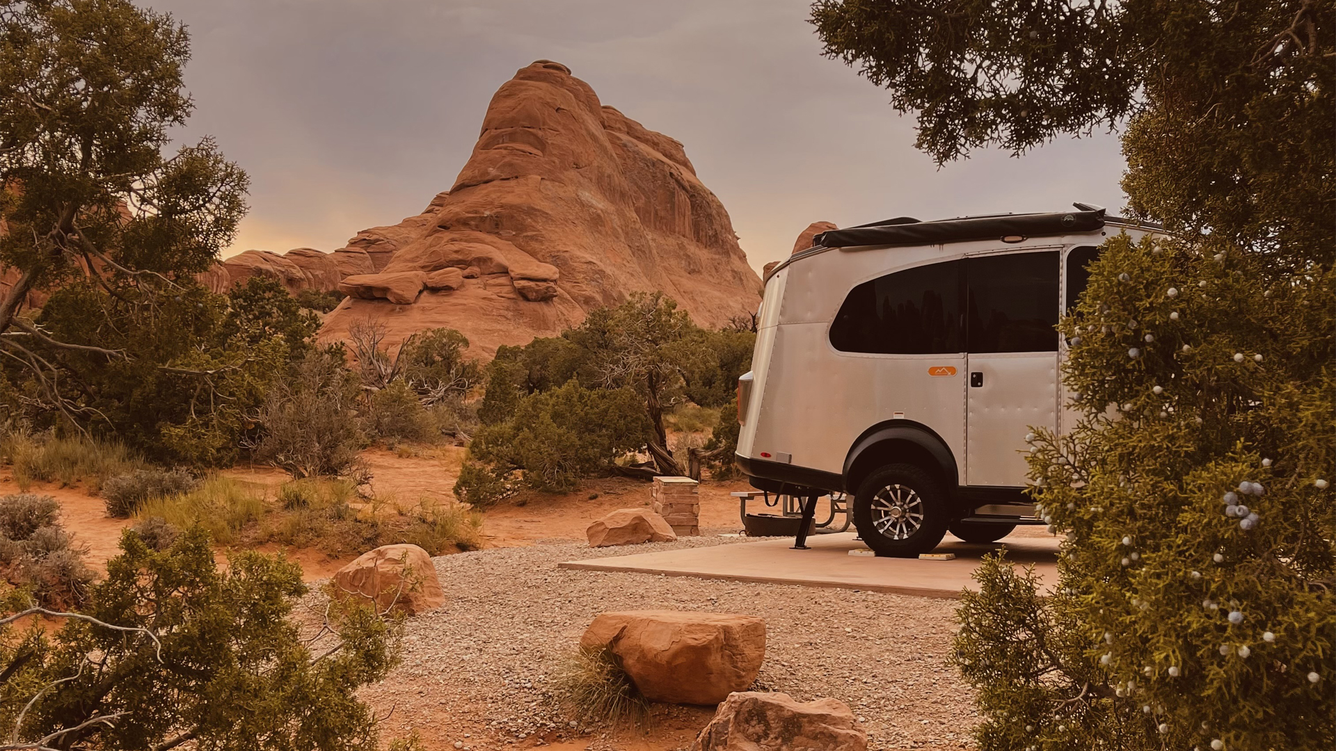 Airstream Basecamp travel trailer parked out west with mountains and trees in the background