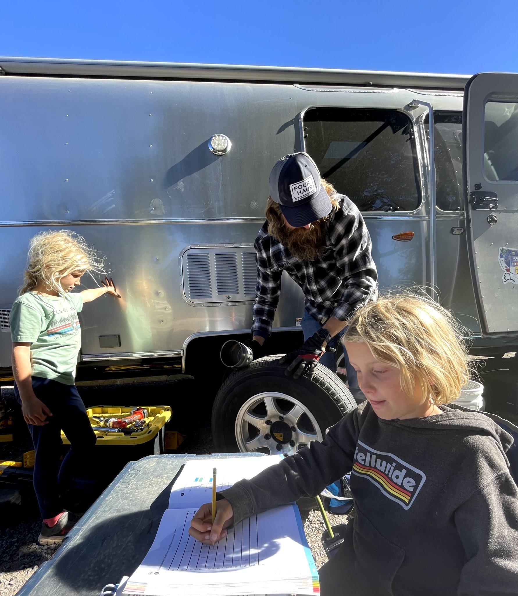 A father and two kids sitting outside of their Airstream travel trailer while they learn and write about their adventures.