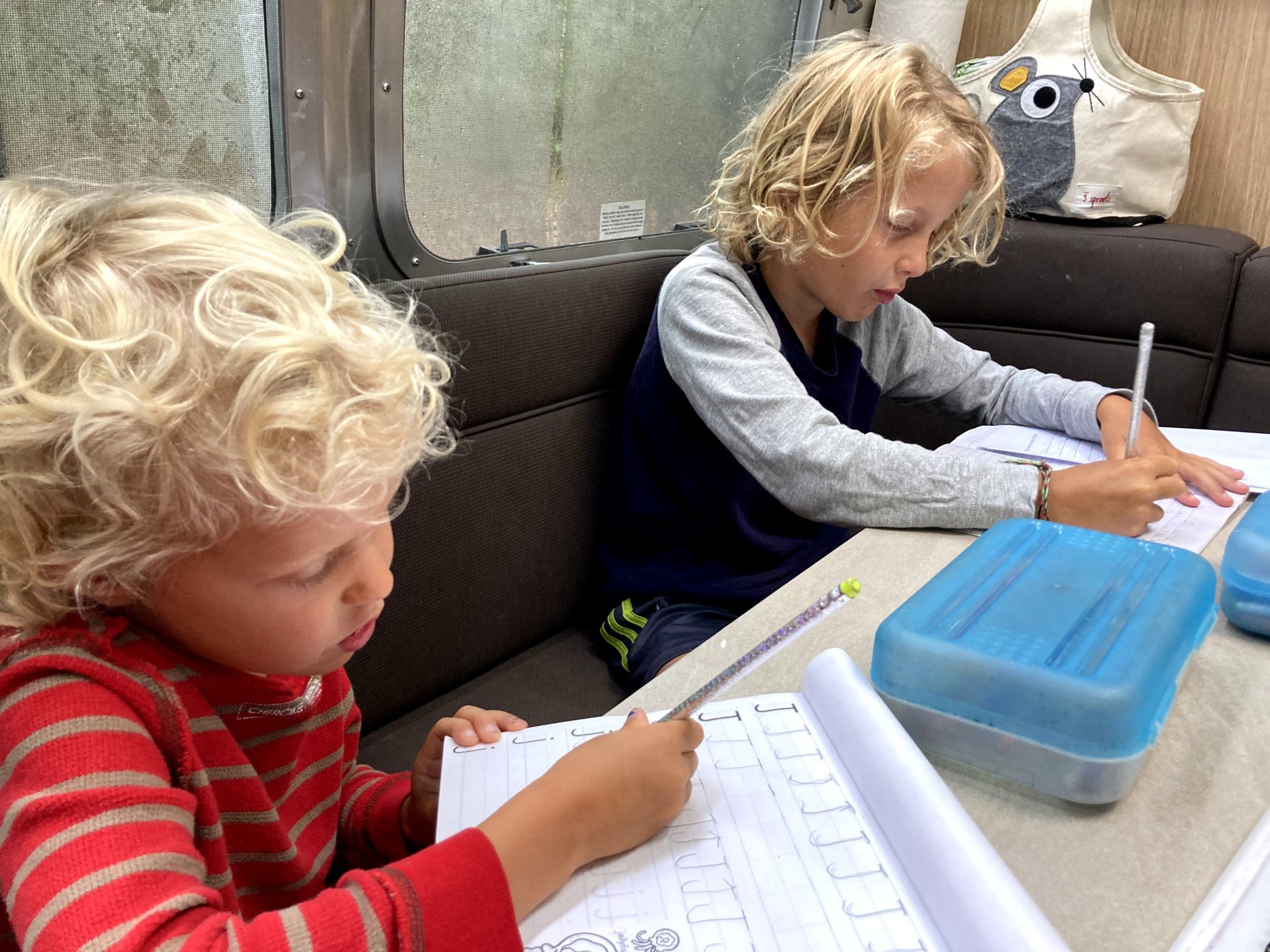 Two kids sitting in the galley of their Airstream travel trailer while they learn on the road.