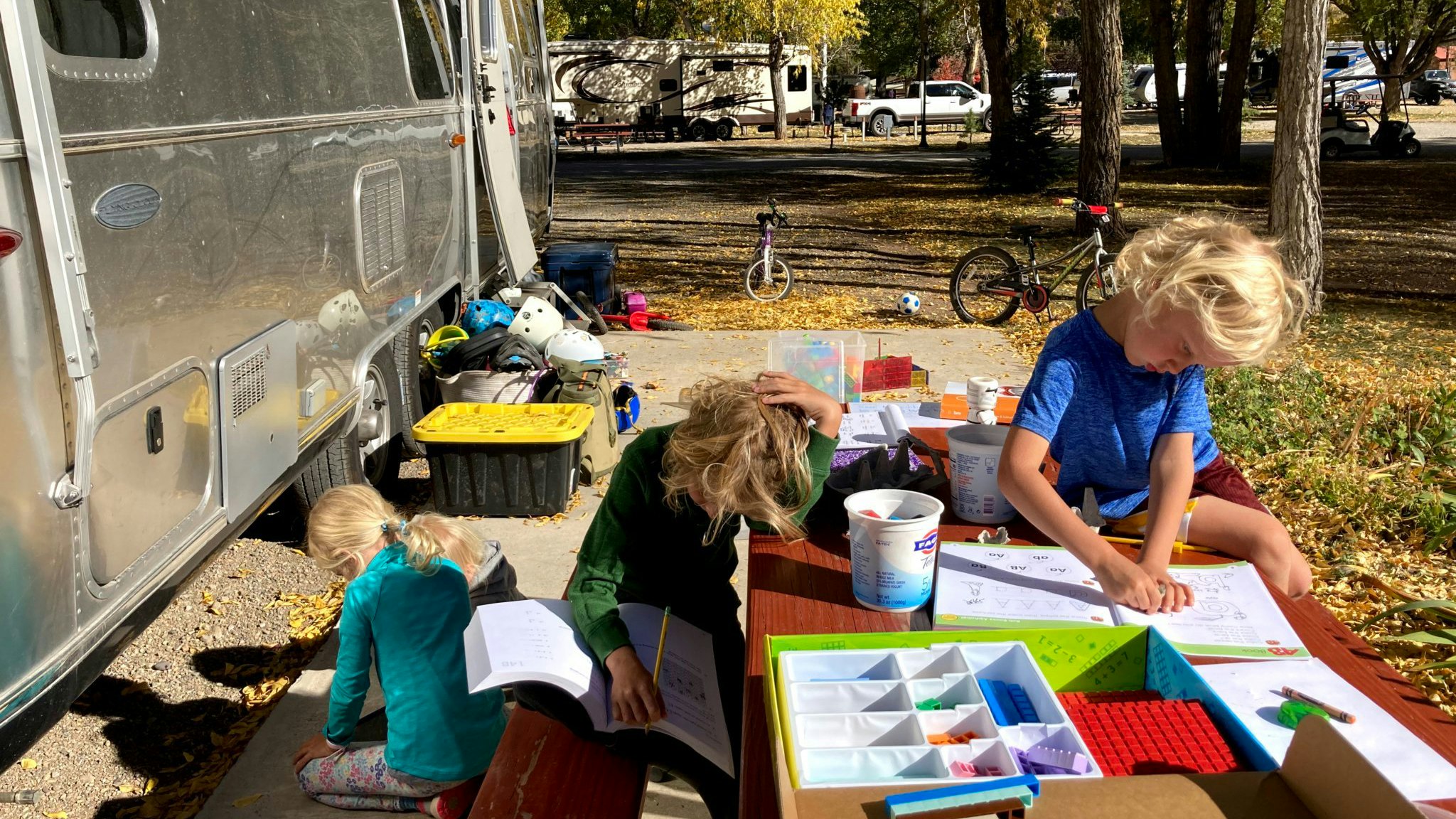 Kids sitting at a table outside of their Airstream travel trailer as they do school on the road.