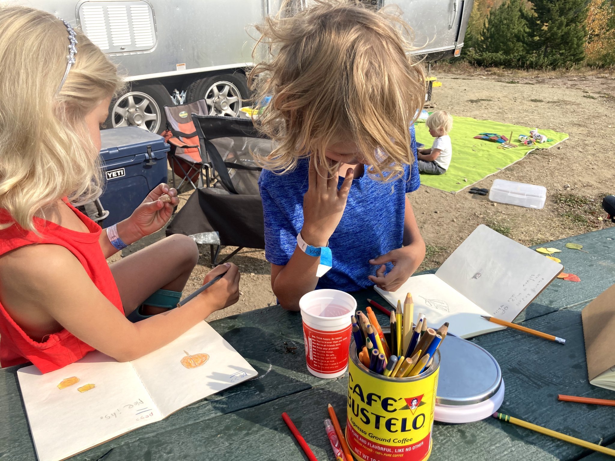 Two kids sitting at a table outside of their Airstream travel trailer while doing crafts.