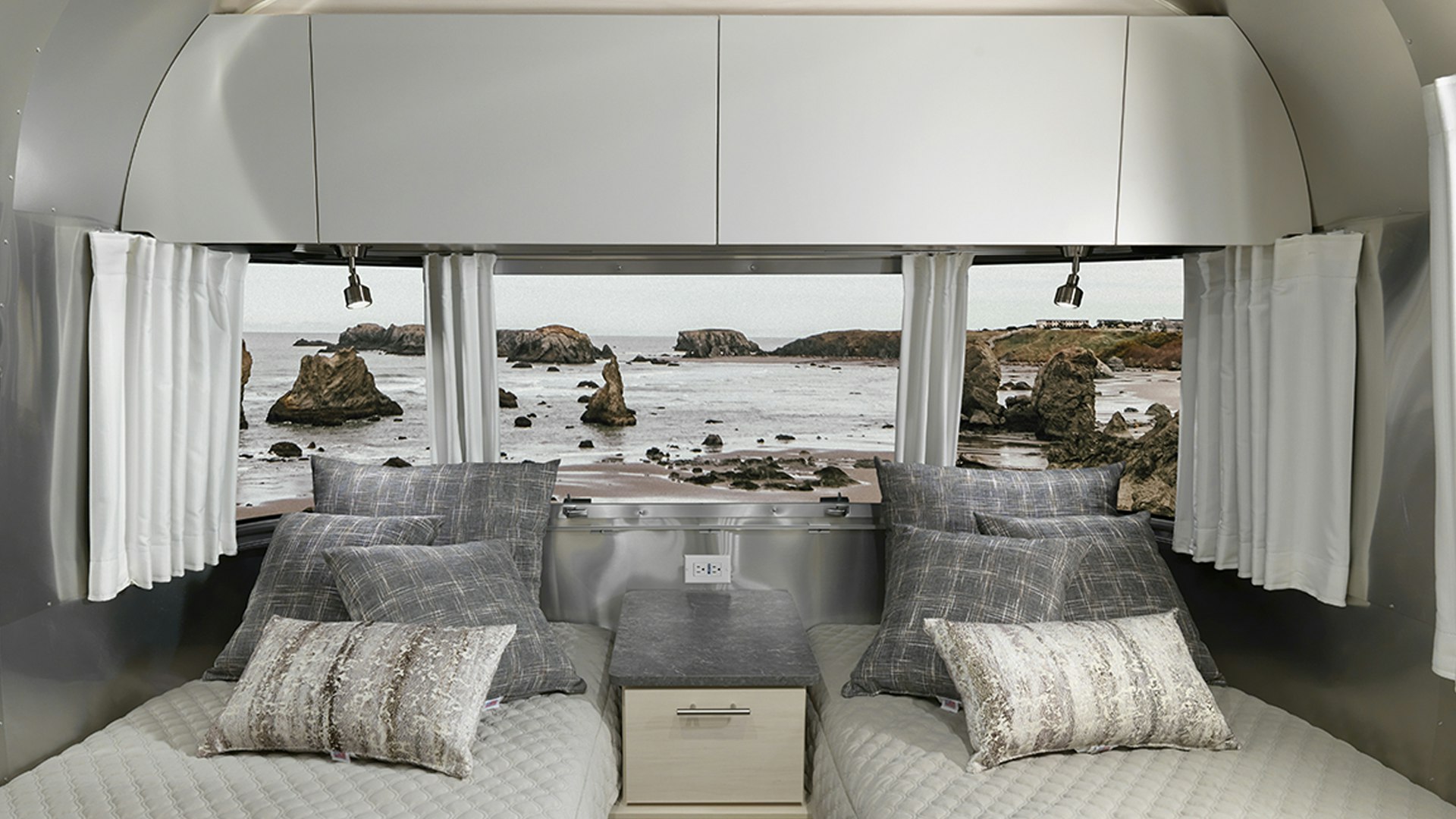 Airstream Flying Cloud 23's bedroom with twin beds while being parked next to a body of water with rocks