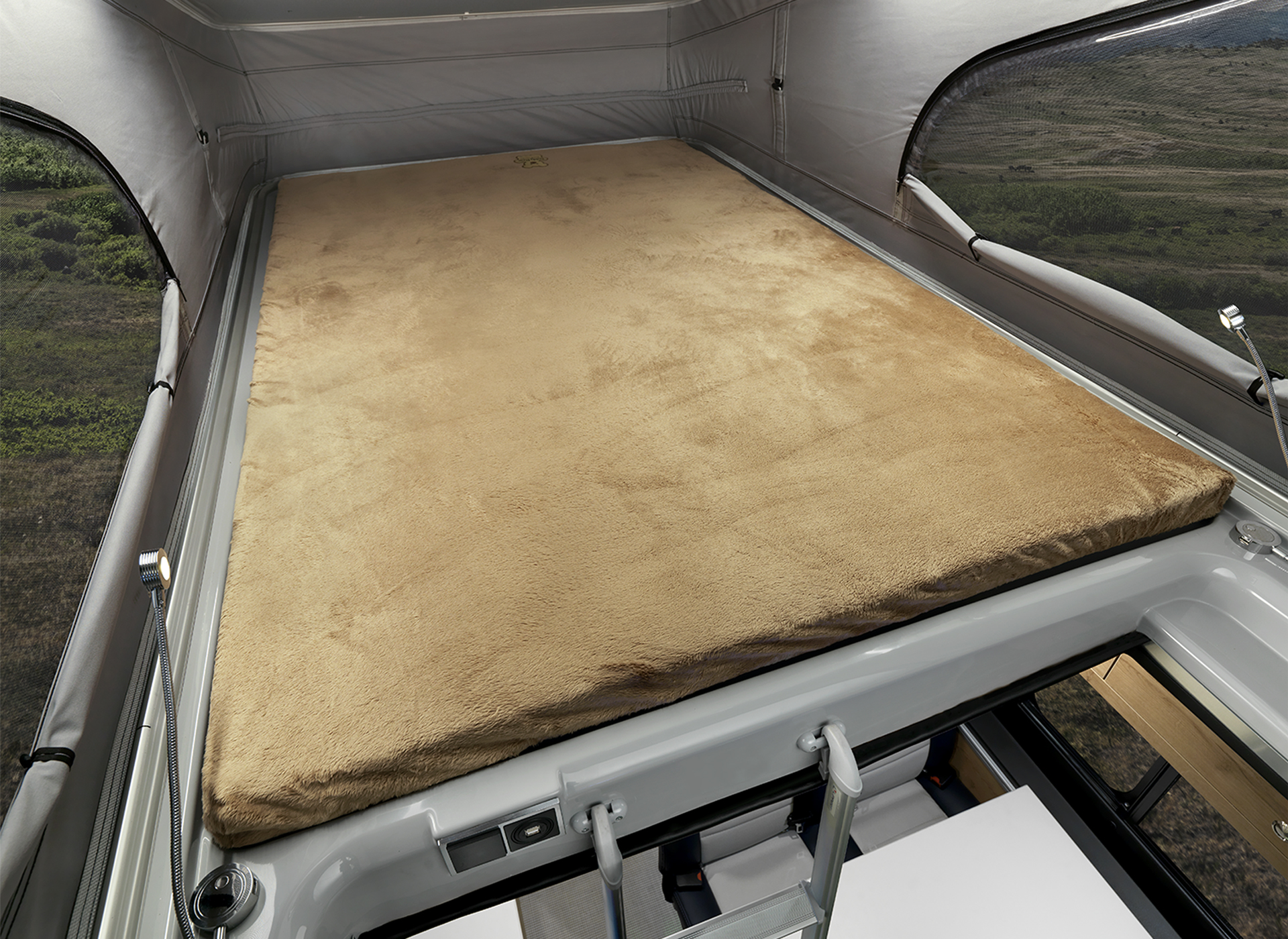 The bed on the interior of the Airstream Rangeline Class B motorhome pop-top with windows looking out at a field and mountains.