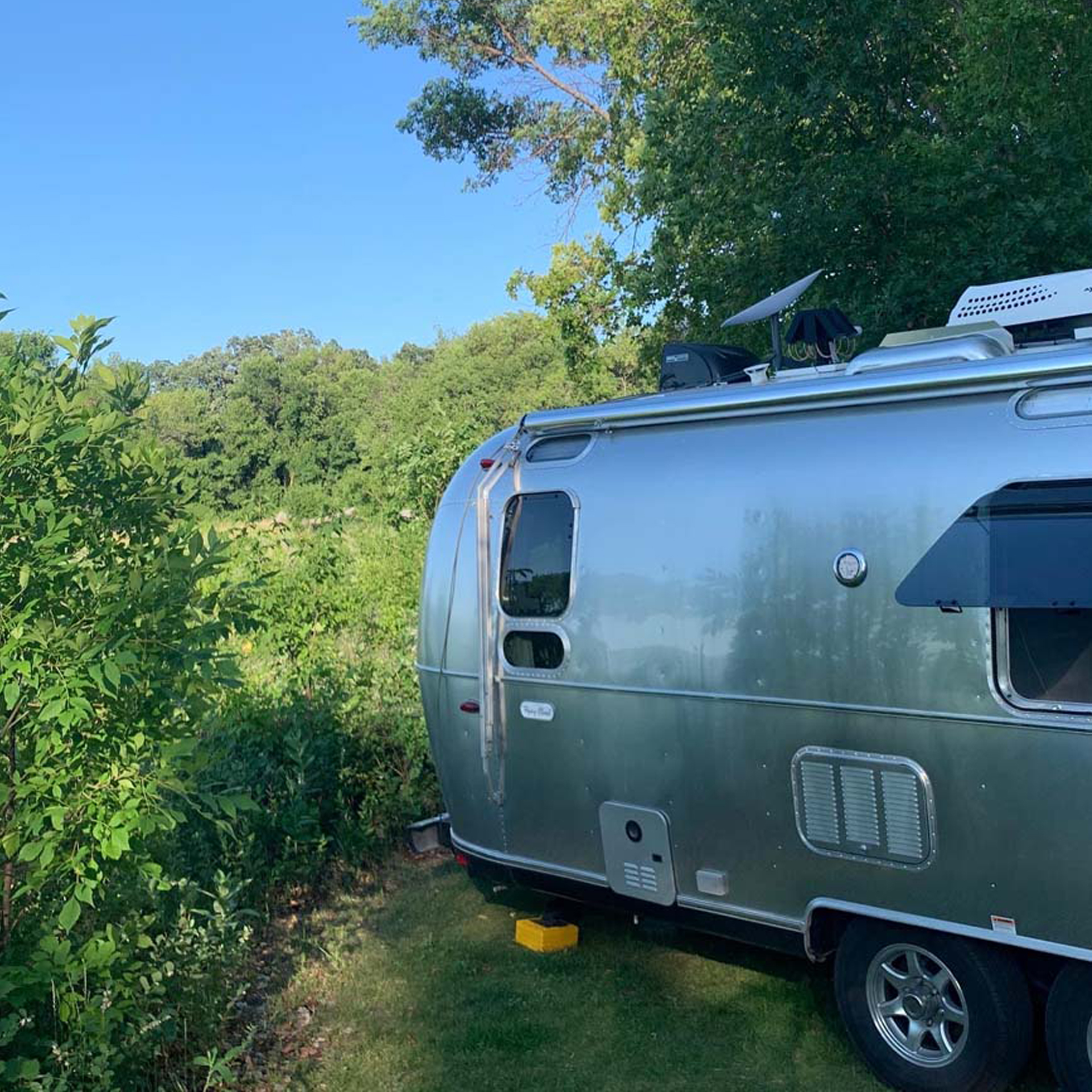 Airstream Flying Cloud camper parked at a campground with trees surrounding the trailer.