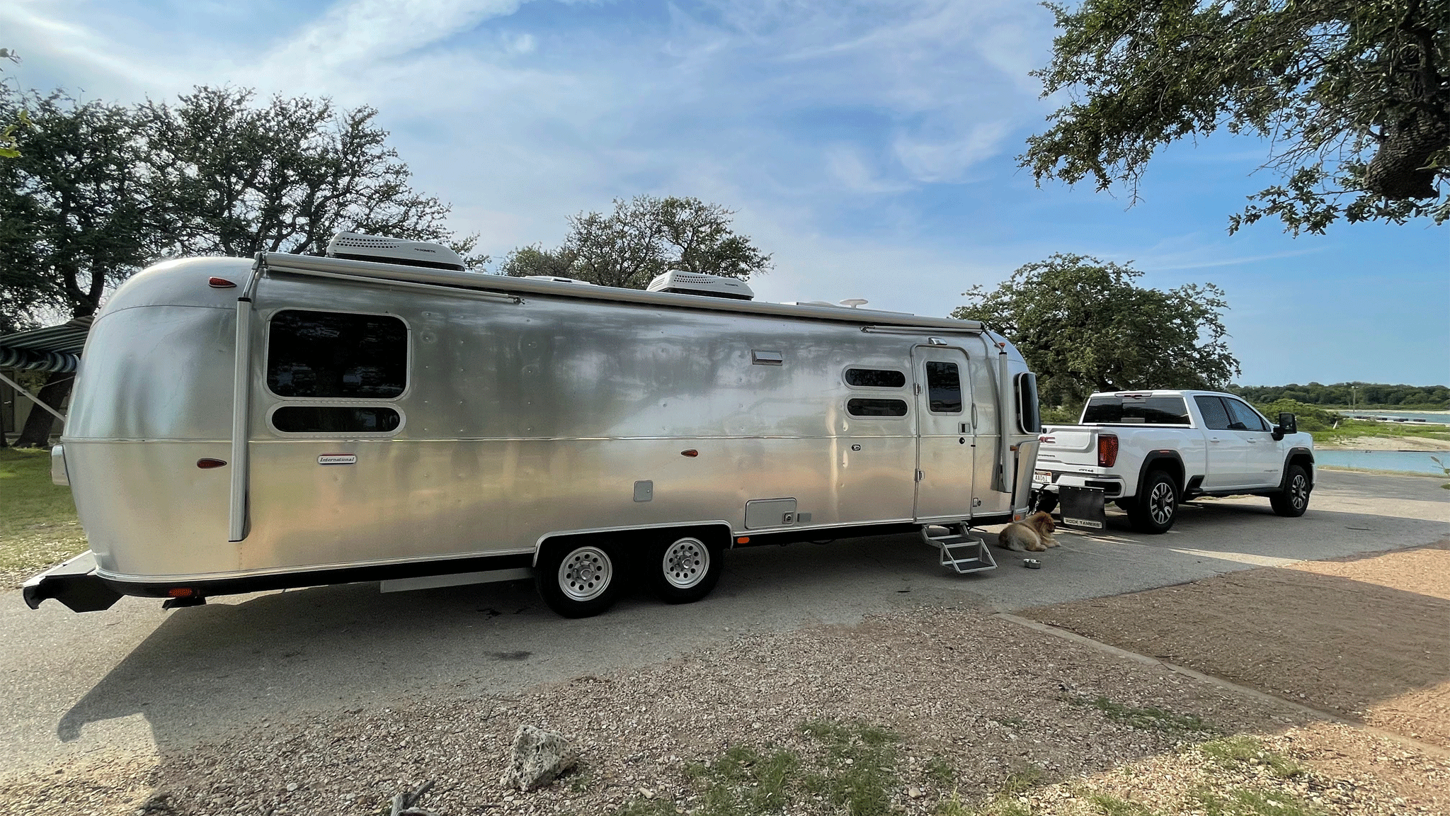 An Airstream International Travel Trailer camper being towed by a white truck down the road.