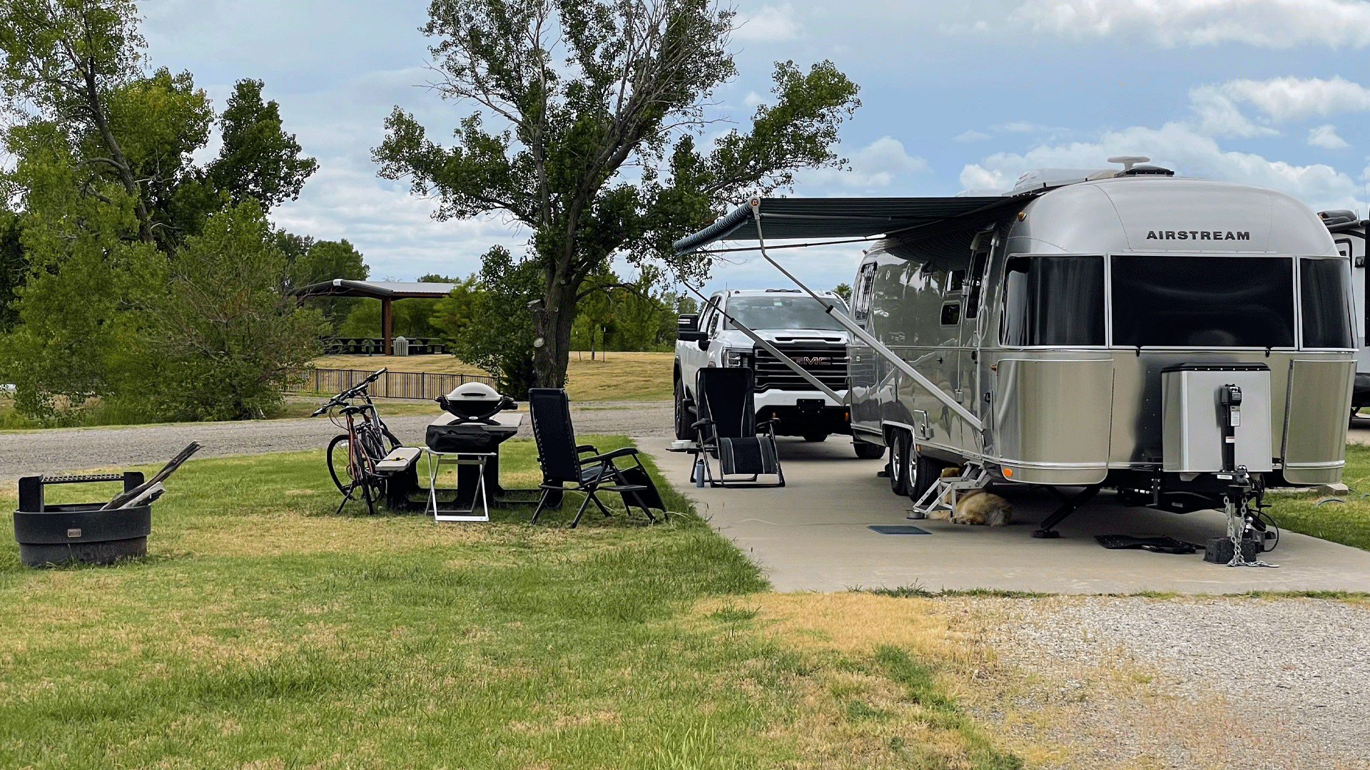 An Airstream camper parked at a campsite in El Dorado with a dog laying under the trailer and a truck parked behind.