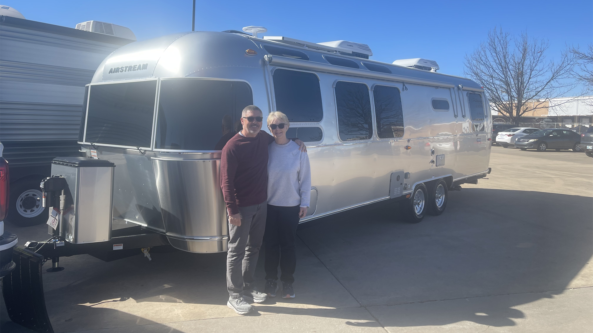 吉姆和苏珊微笑着在他们的新Airstream国际旅行房车露营车旁边拍照。