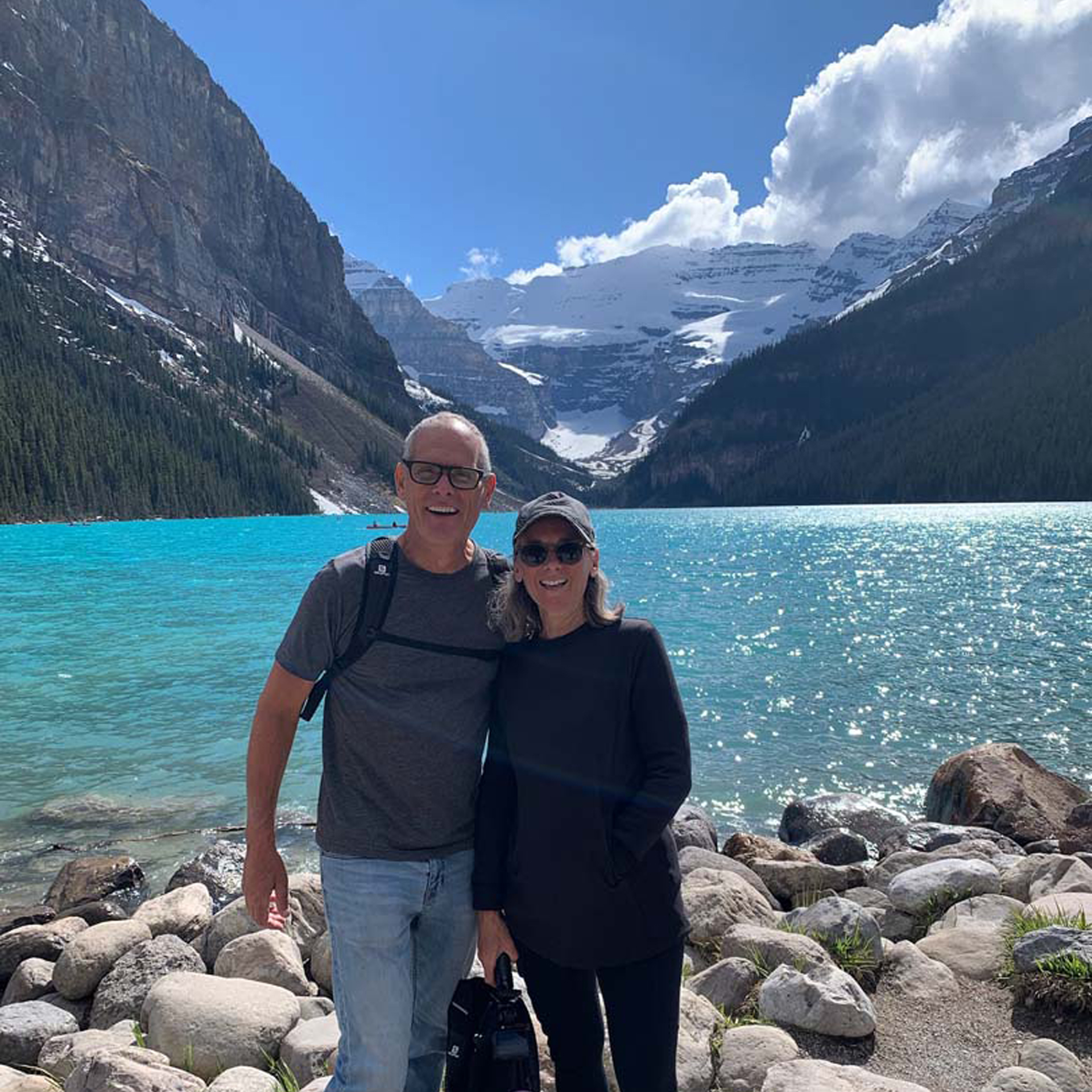 Scott and Kim posing for an image next to a lake and mountains.