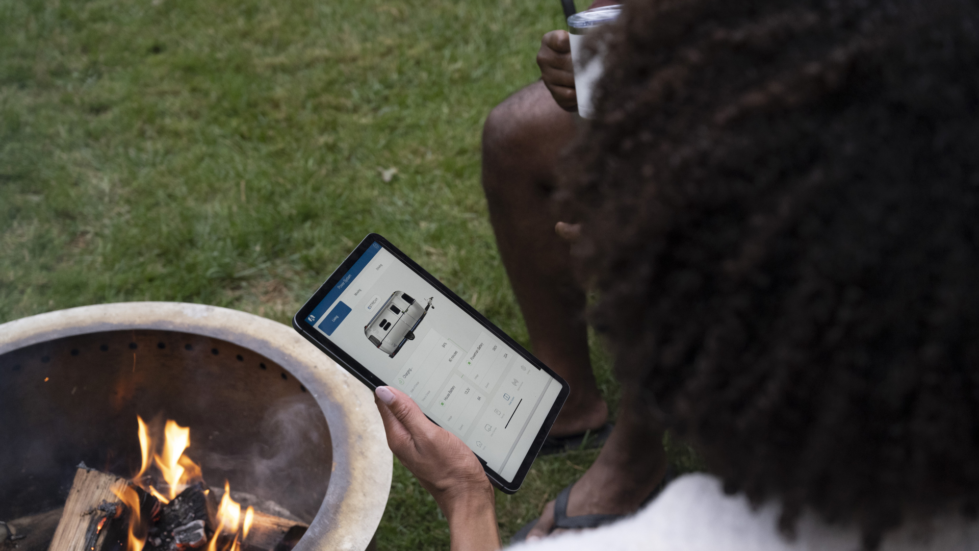 Two people parking the Airstream eStream travel trailer from an iPad while sitting by a campfire.