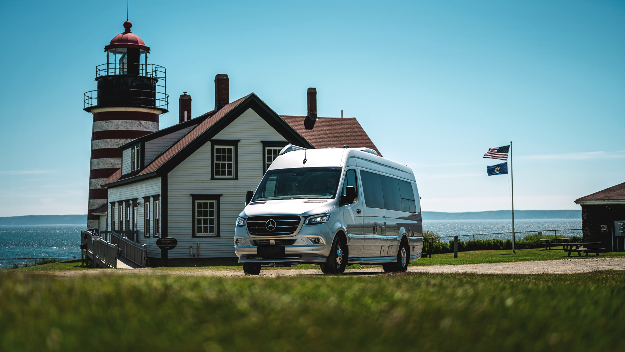 Airstream Interstate 24 Class B Motorhome parked outside a lighthouse with flags flying in the background.