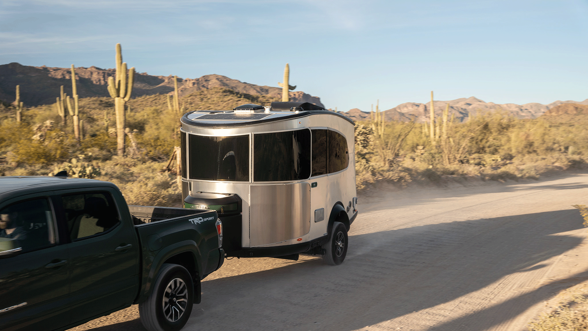 The Airstream REI Co-op Special Edition Travel Trailer being towed by a green truck down a dirt road in Sedona, Arizona.