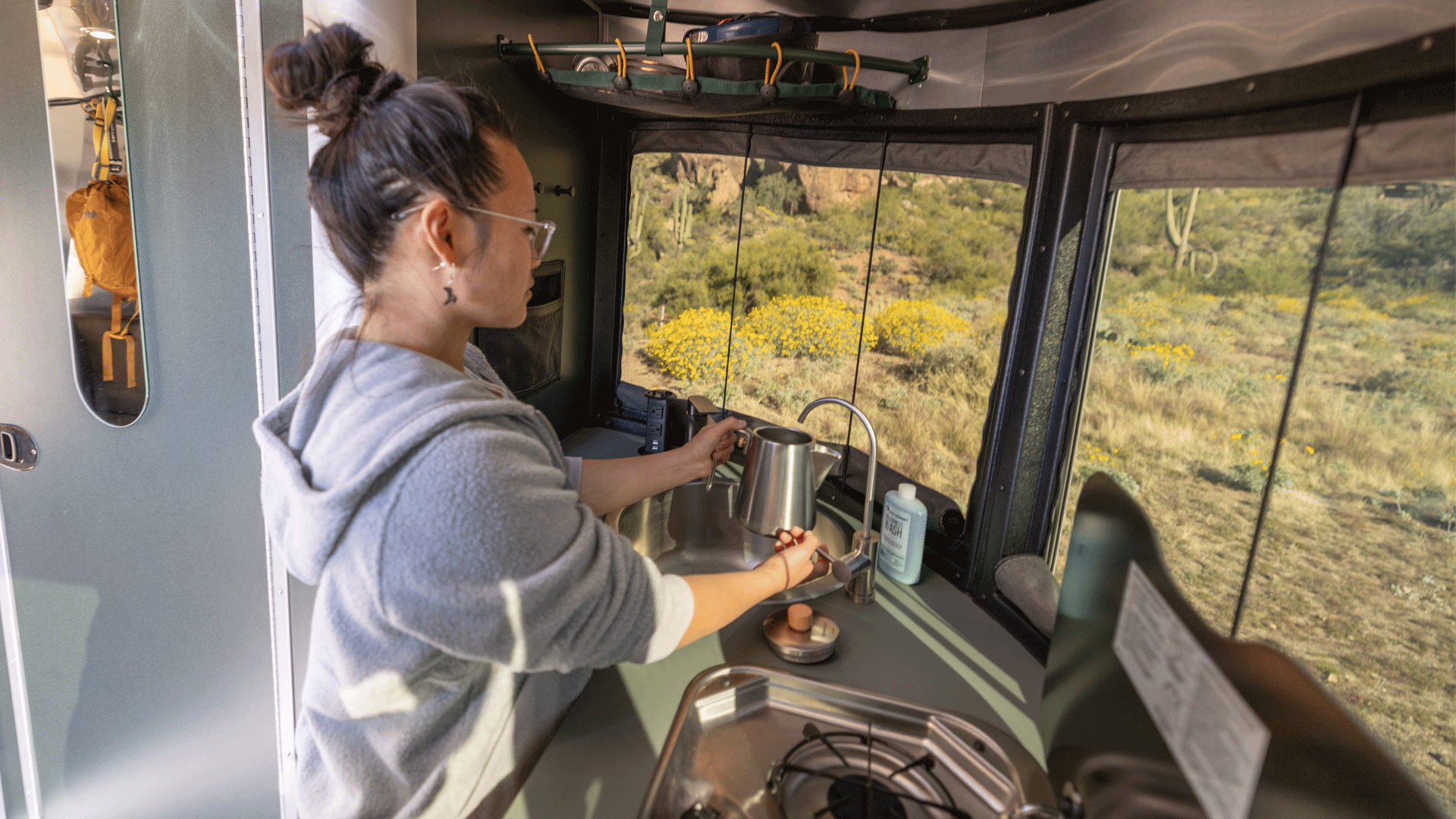 A woman filling up a coffee pot in her Airstream REI Co-op Special Edition Travel Trailer while she camps in Arizona.