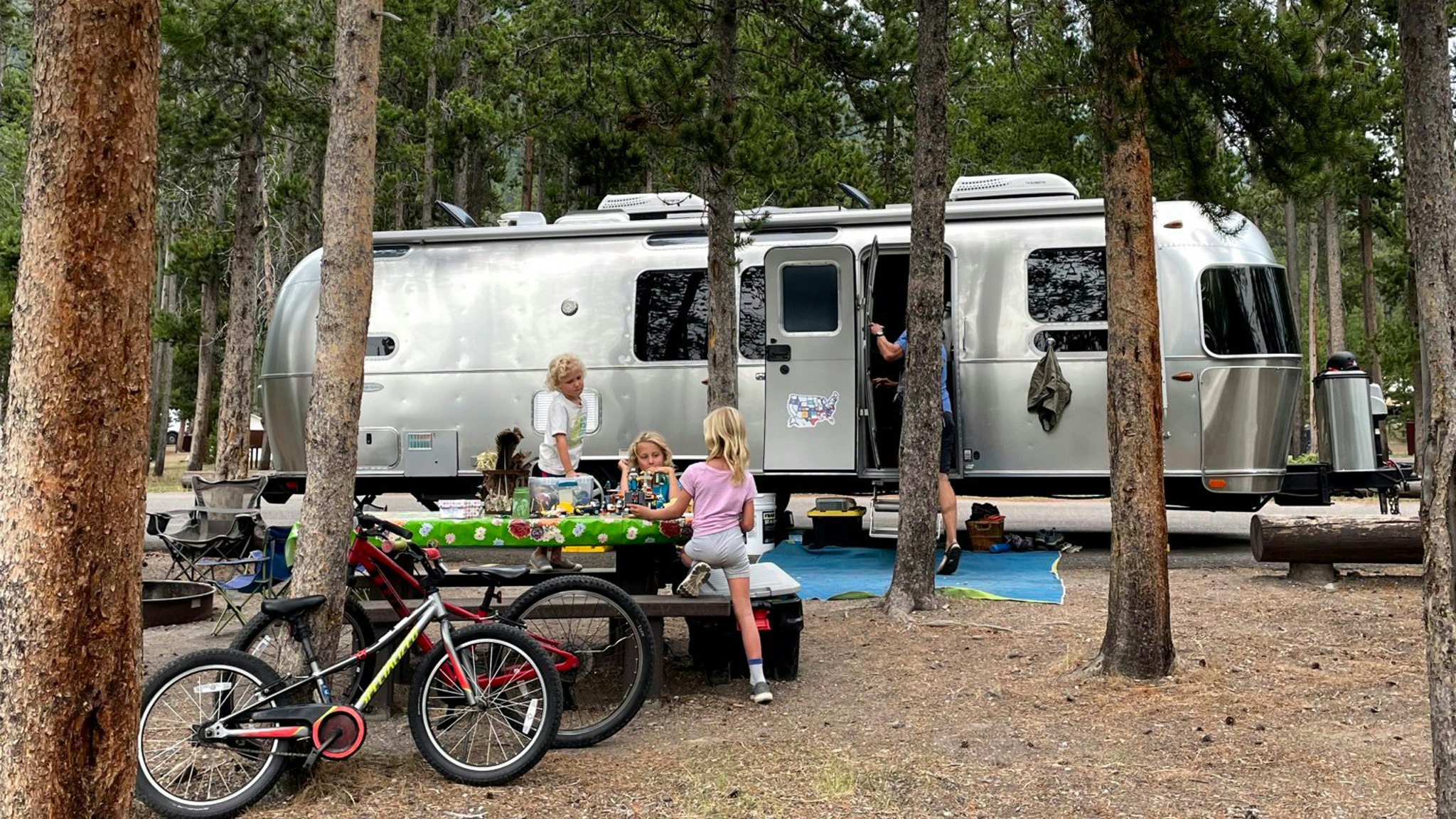 孩子们坐在野餐桌上，在他们露营时在他们的气流旅行拖车外面玩。