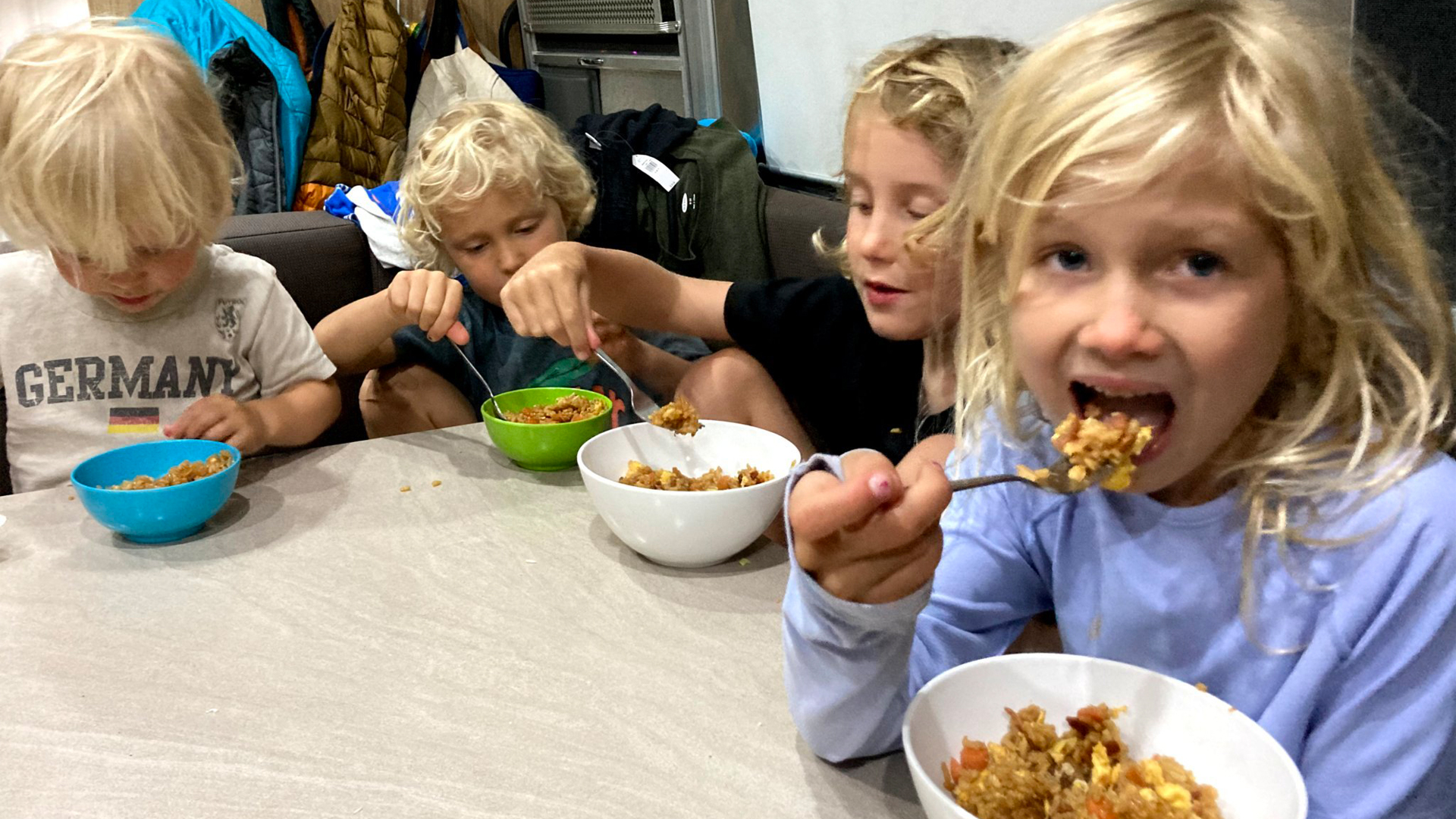 四个孩子坐在一辆气流旅行拖车的桌子旁，一边露营一边吃晚饭。