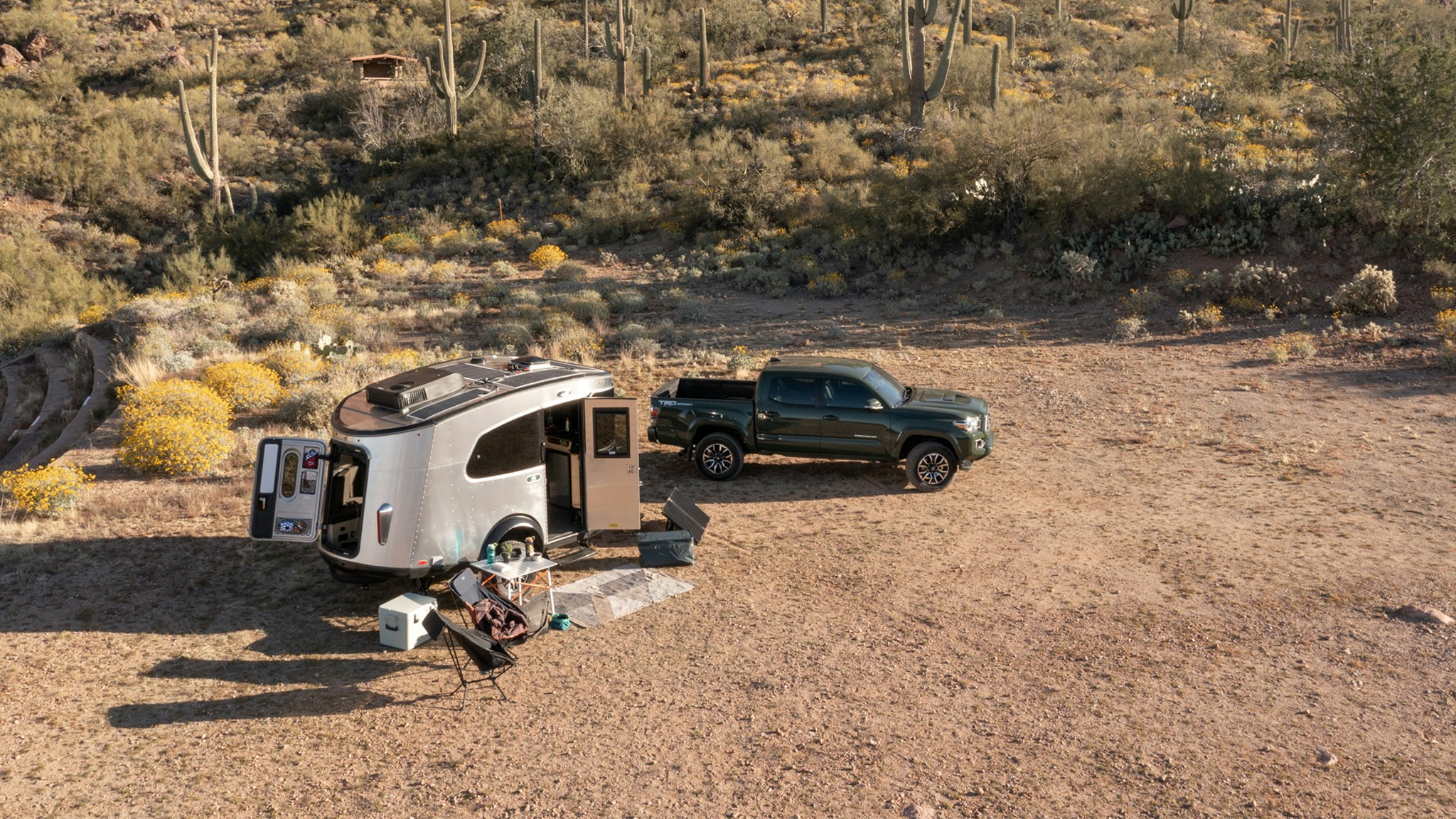 An Airstream REI Co-op Basecamp travel trailer parked at a spot in Arizona with the campsite set up and a green truck parked next to the camper.